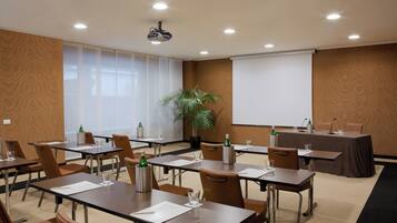 A conference room with tables, chairs, a projector, and a screen.