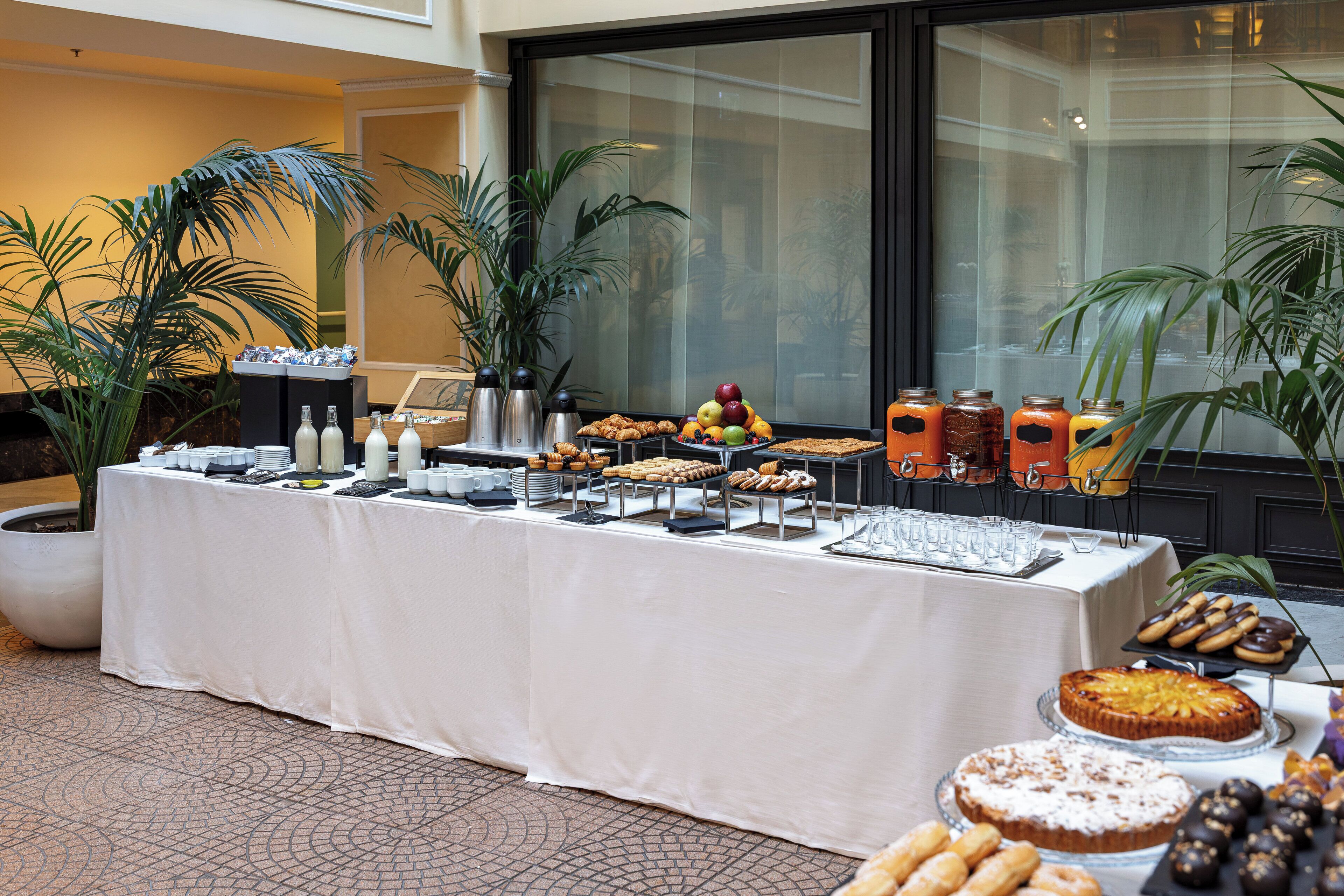Une table de buffet garnie de divers plats et boissons, entourée de plantes en pot.