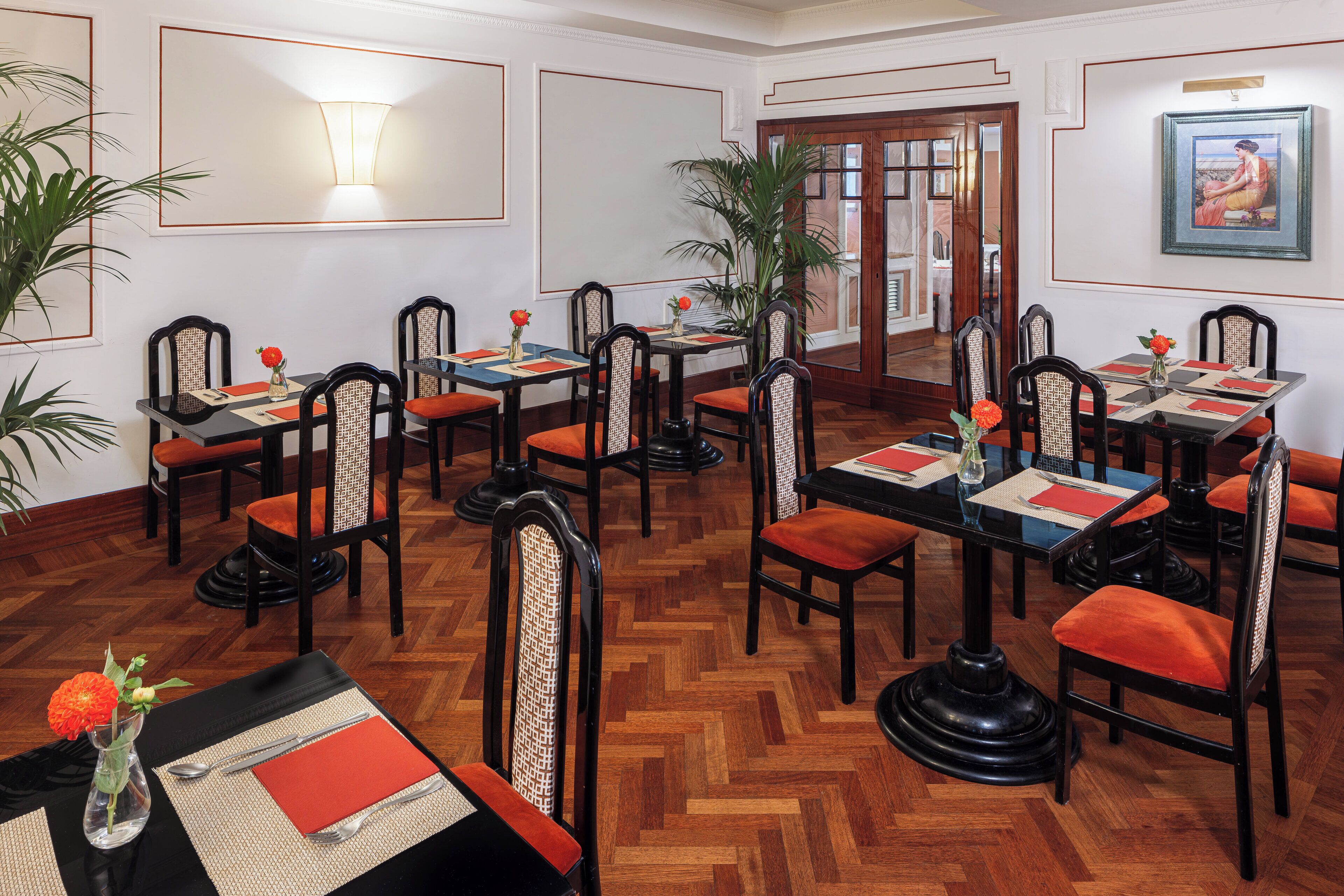 A dining area with multiple tables and chairs, each set with place settings and small potted plants.