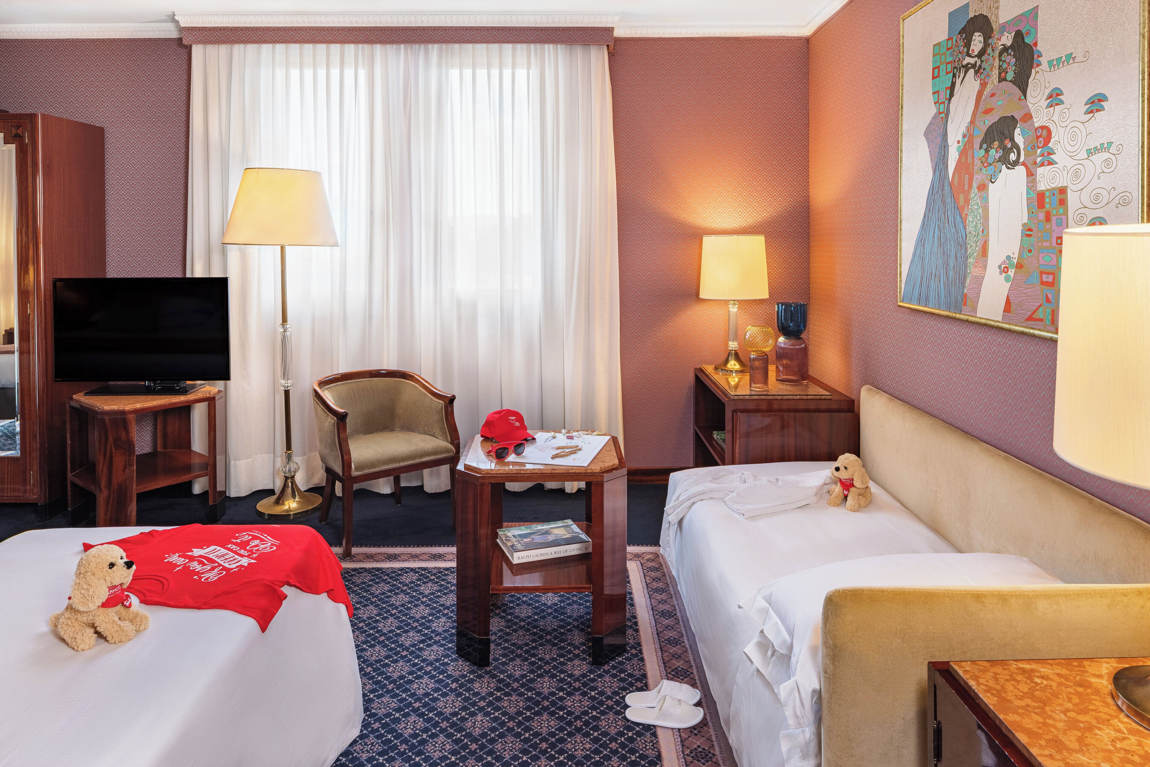 Hotelkamer met twee bedden, een televisie, een stoel, een tafel met lamp en een schilderij aan de muur.