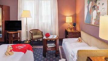 Hotelkamer met twee bedden, een televisie, een stoel, een tafel met lamp en een schilderij aan de muur.