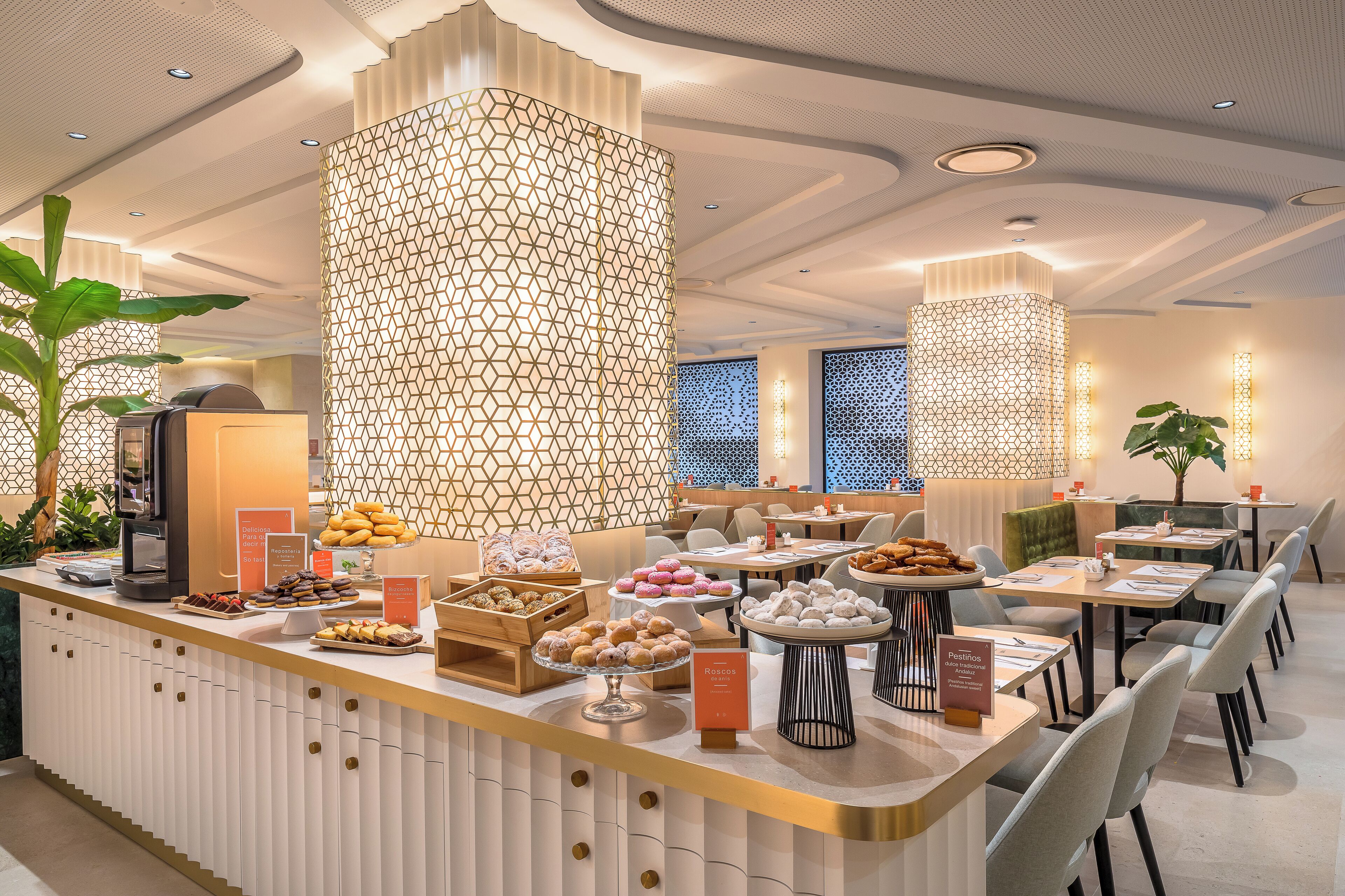 A modern hotel lobby with a central counter displaying pastries and a geometric patterned wall.