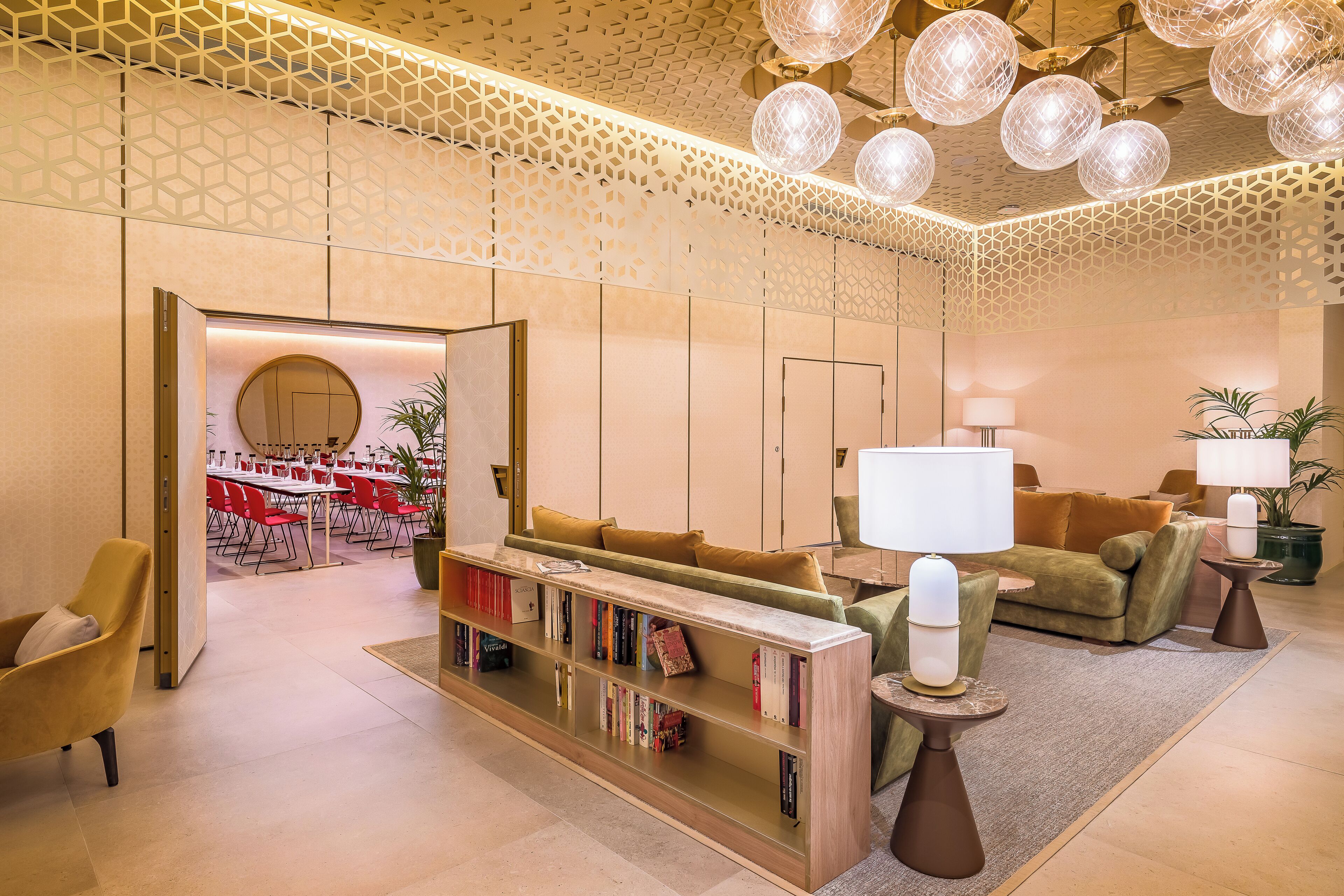A modern lobby with a seating area, a bookshelf, and a dining area in the background.