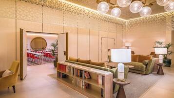 A modern lobby with a seating area, a bookshelf, and a dining area in the background.