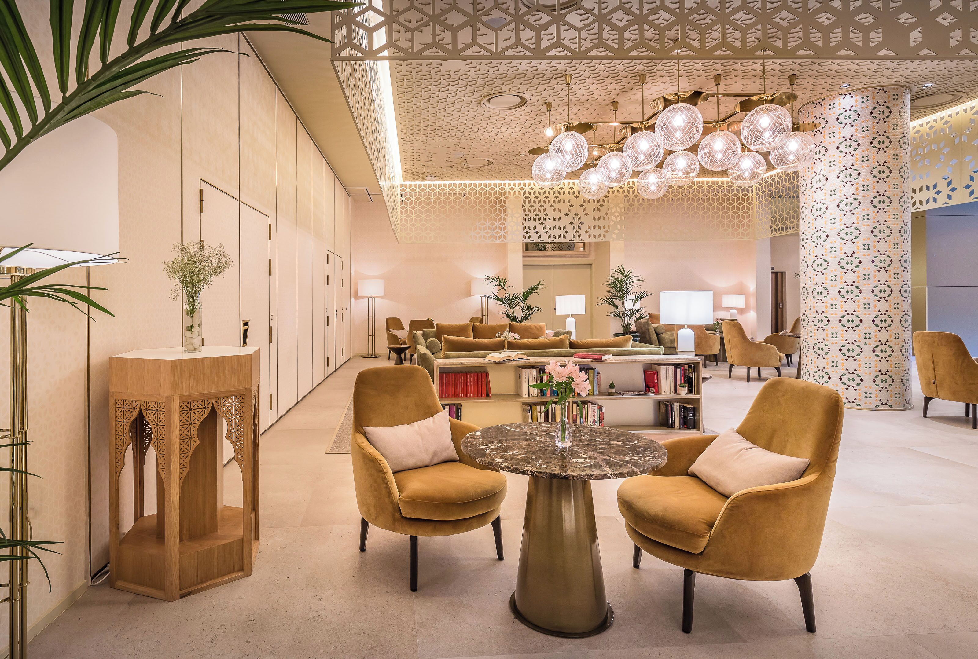 A spacious lobby with a modern design, featuring a round table with chairs, a decorative wooden stand, and a patterned column.