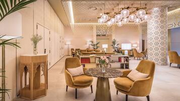 A spacious lobby with a modern design, featuring a round table with chairs, a decorative wooden stand, and a patterned column.