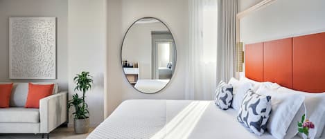 A modern hotel room with a large bed, a sofa, a potted plant, and a mirror.