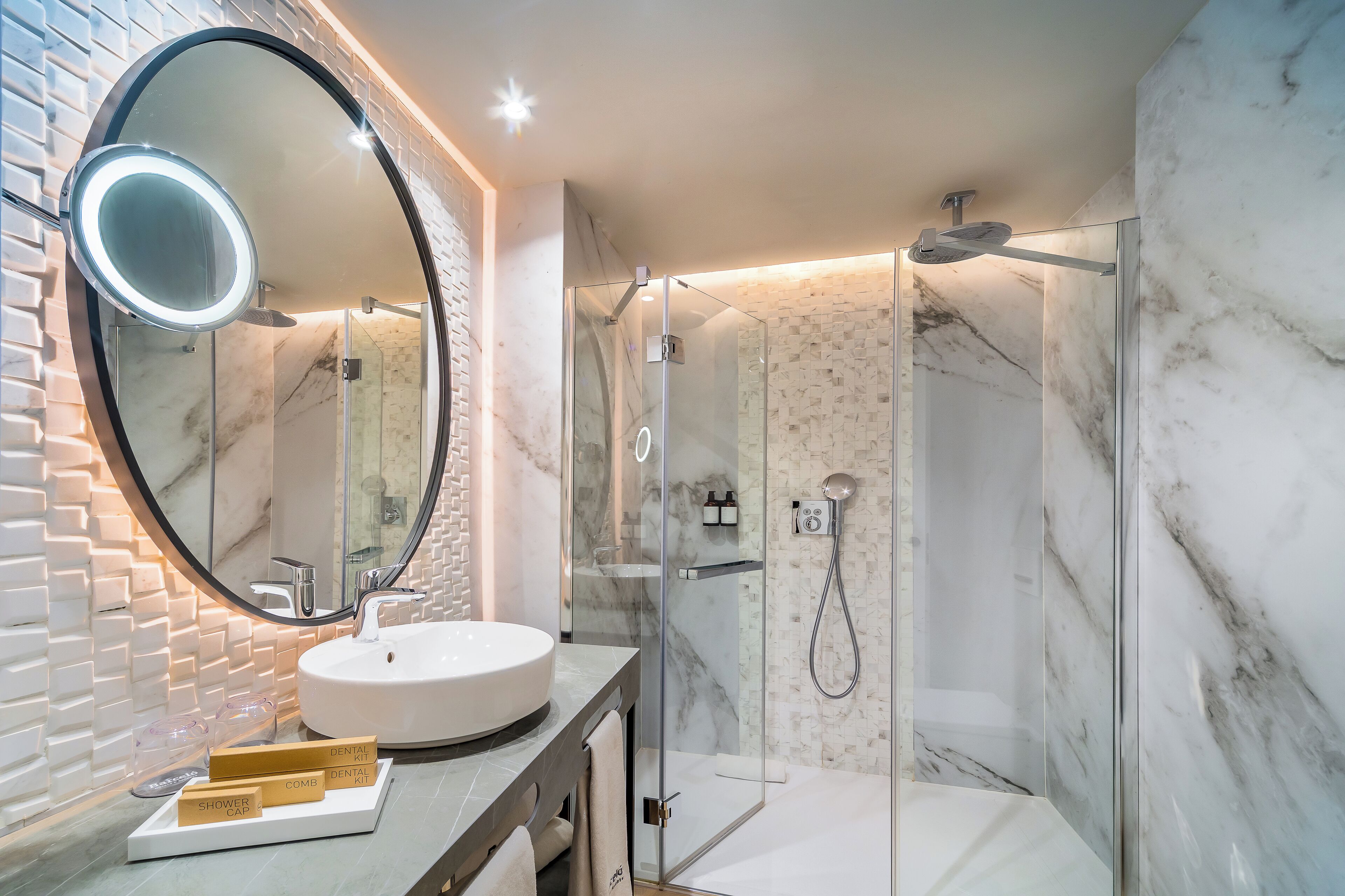A modern bathroom with a round mirror, white sink, and glass shower enclosure.