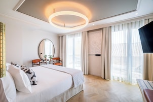 A modern hotel room with a large bed, a round mirror, a desk with two chairs, and a TV on a stand.