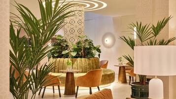 Un espace de détente moderne avec une table ronde, un canapé et plusieurs fauteuils. On y trouve également plusieurs plantes en pot et une lampe.