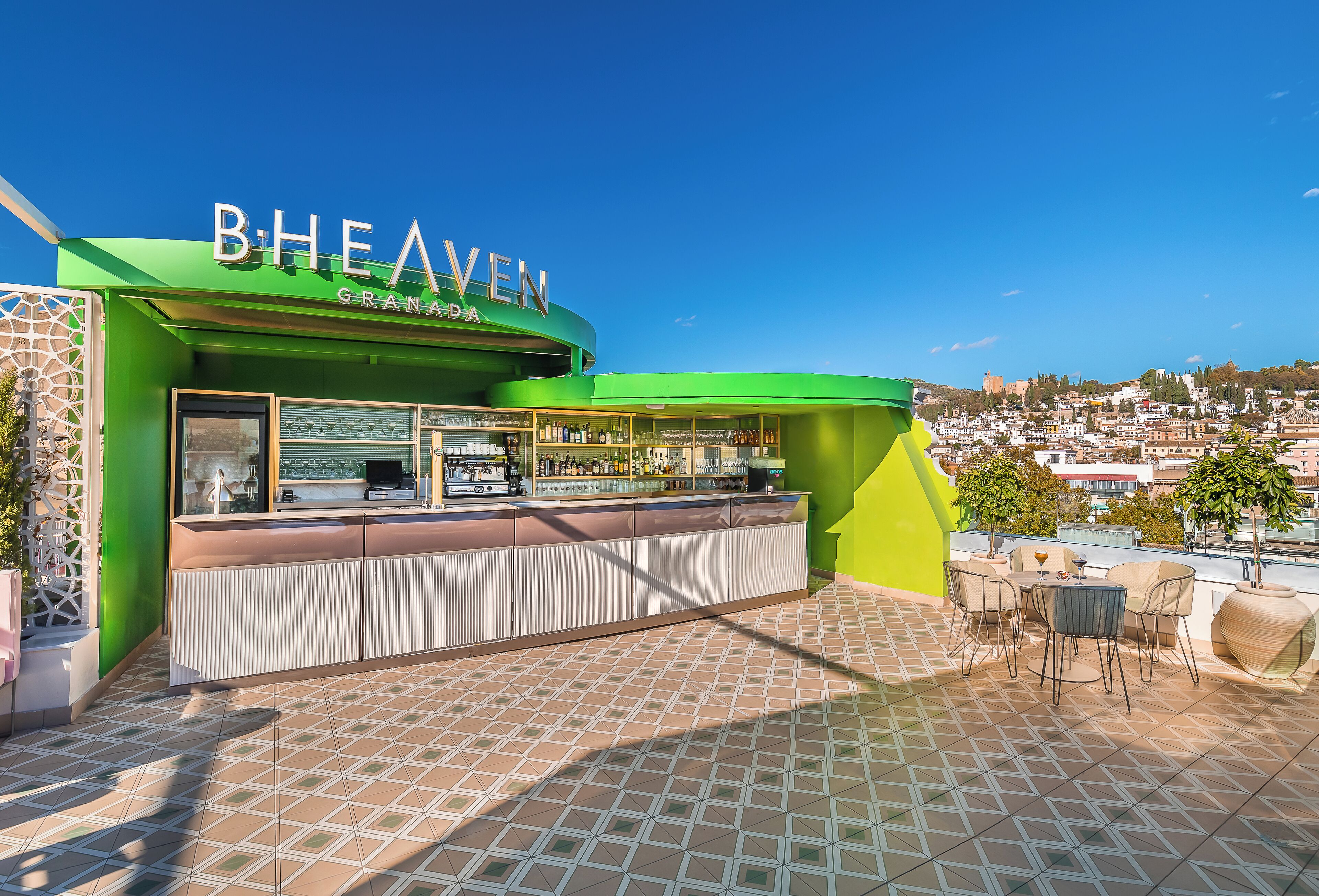 A green outdoor bar area with a tiled floor and a view of the city in the background.