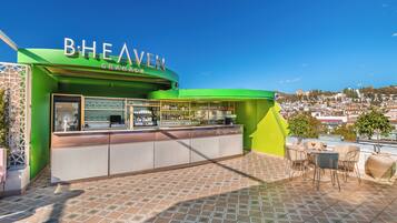 A green outdoor bar area with a tiled floor and a view of the city in the background.