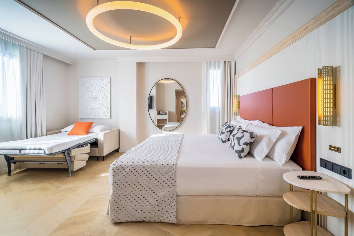 A hotel room with a bed, bedside table, and a small seating area with a chair.