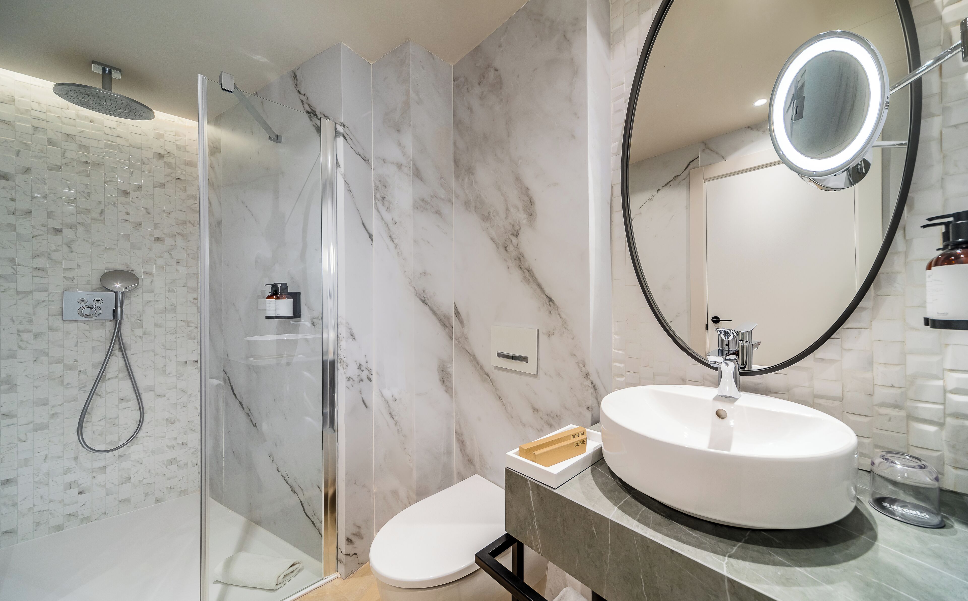 A modern bathroom with a glass-enclosed shower, a round sink with a marble countertop, and a large mirror.