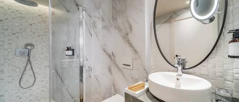 A modern bathroom with a glass-enclosed shower, a round sink with a marble countertop, and a large mirror.