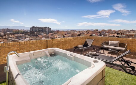 A rooftop terrace with a hot tub, lounge chairs, and a view of a cityscape.
