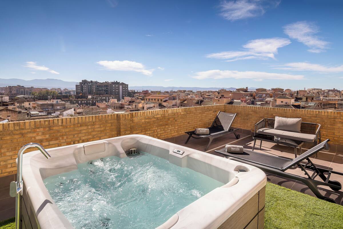A rooftop terrace with a hot tub, lounge chairs, and a view of a cityscape.