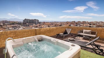 Una terraza en la azotea con jacuzzi, sillas de descanso y vistas a un paisaje urbano.