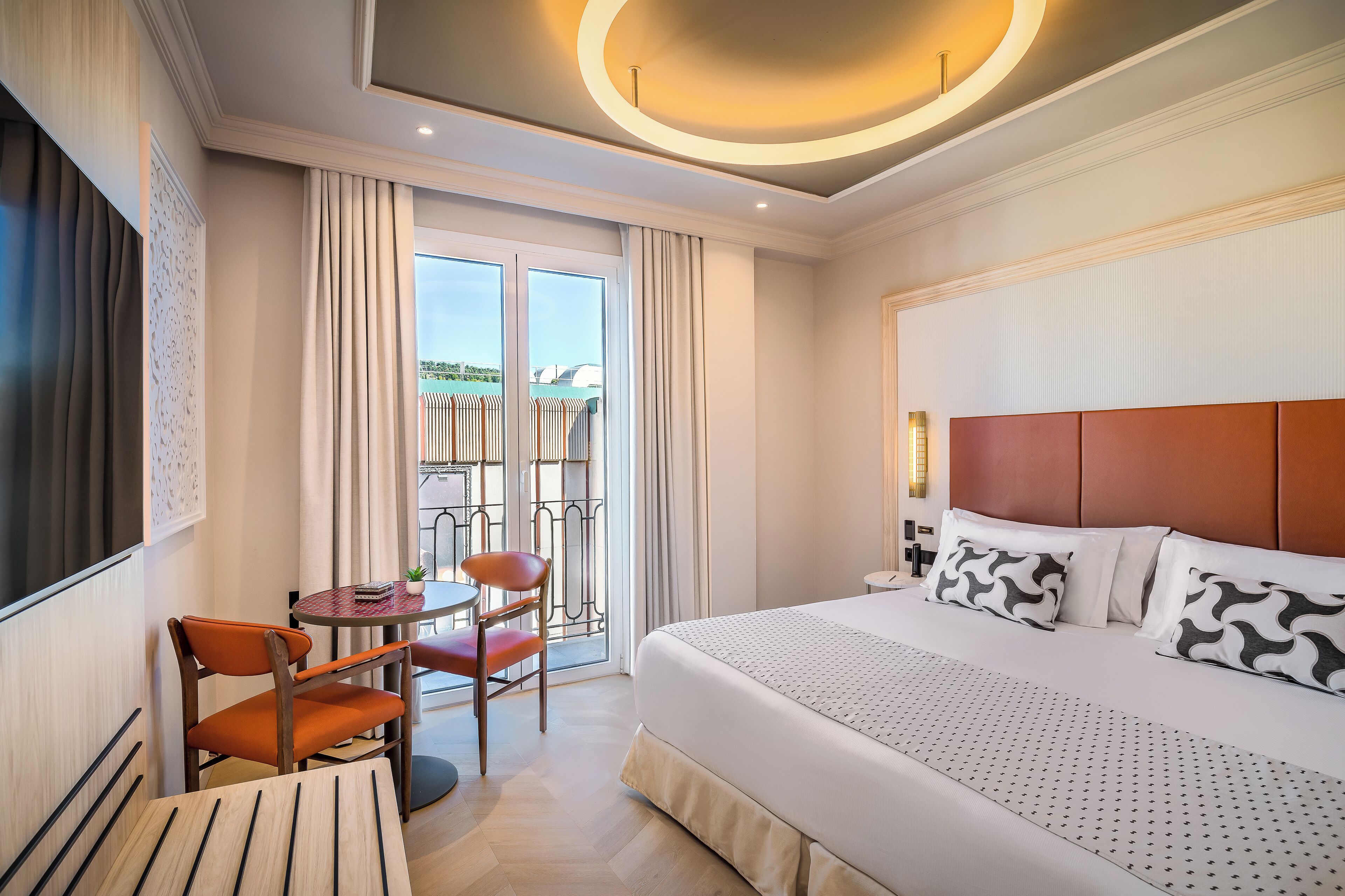 Ein Hotelzimmer mit einem großen Bett, einem kleinen Tisch mit Stühlen, einem Fernseher und einem Balkon mit Aussicht.
