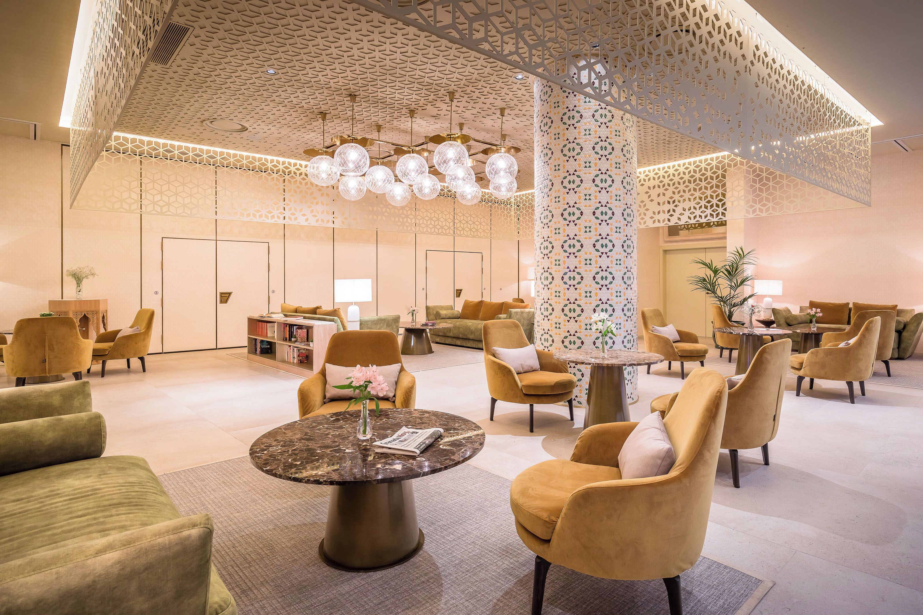 A spacious lobby with modern furniture, a central round table, and decorative lighting.