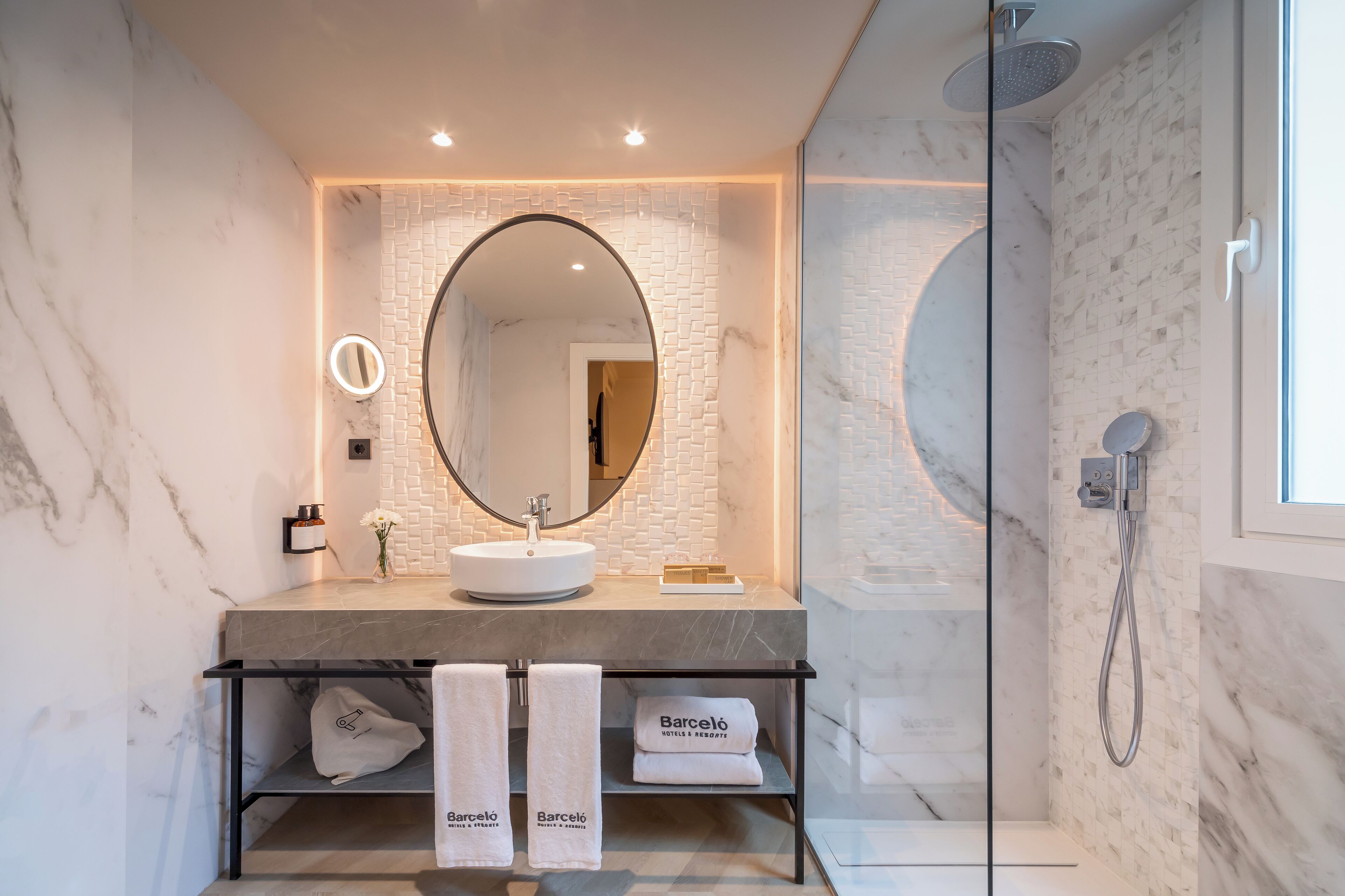 Un baño moderno con un lavabo de mármol, un espejo grande y una ducha con cerramiento de vidrio.