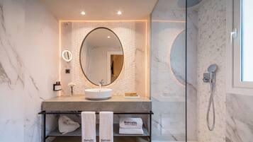 Un baño moderno con un lavabo de mármol, un espejo grande y una ducha con cerramiento de vidrio.
