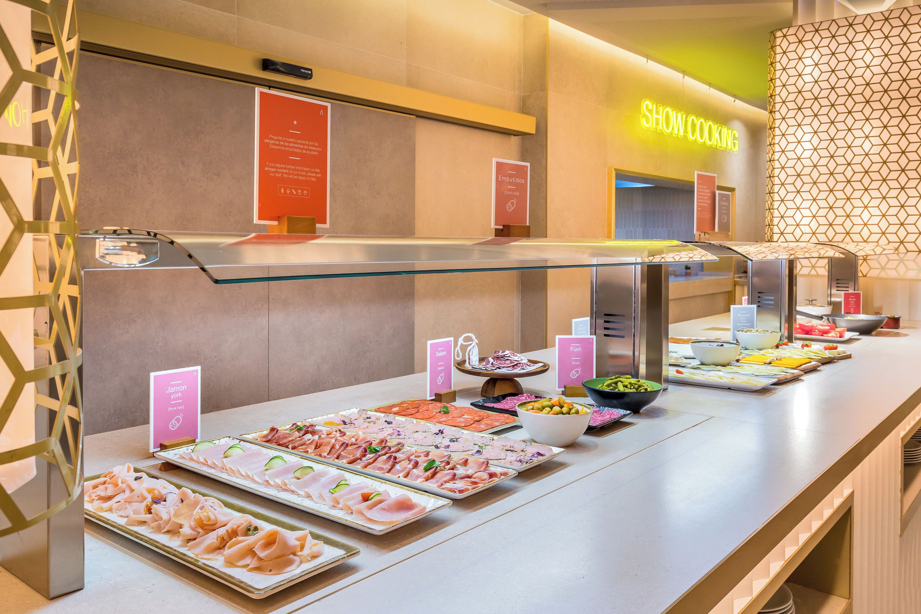 A buffet area with various food options, a 'Show Cooking' sign, and a 'Jamón y queso' sign.