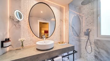Un baño moderno con un espejo redondo, un lavamanos blanco y una ducha con mampara de vidrio.