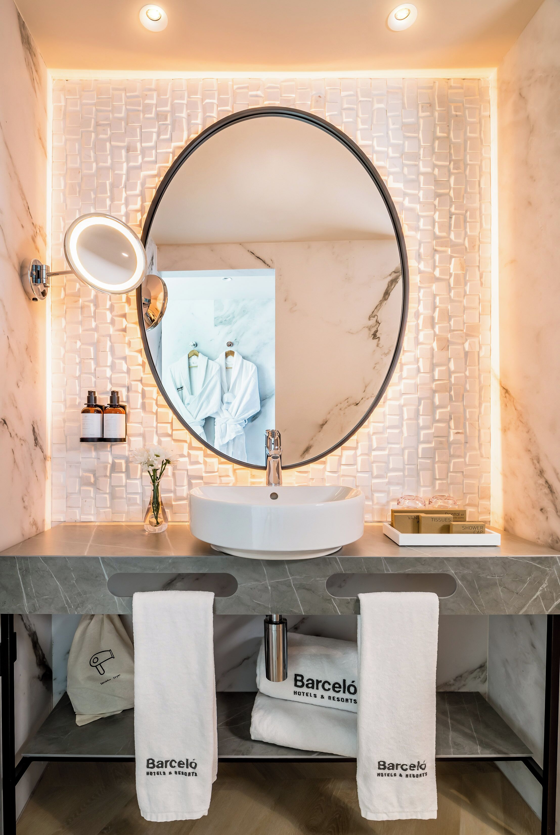 A modern bathroom with a round mirror, white marble sink, and a towel rack with towels.
