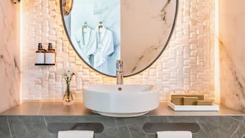 Un baño moderno con un espejo redondo, lavabo de mármol blanco y un perchero con toallas.