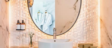 A modern bathroom with a round mirror, white marble sink, and a towel rack with towels.