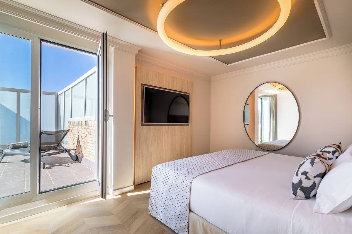 A modern bedroom with a large bed, a TV, and a sliding glass door leading to an outdoor area.