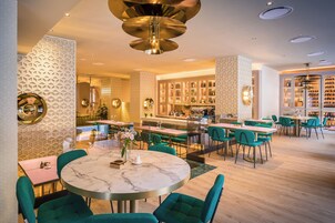 Un restaurante moderno con mesas redondas, sillas verdes y una zona de bar con estantes llenos de botellas.