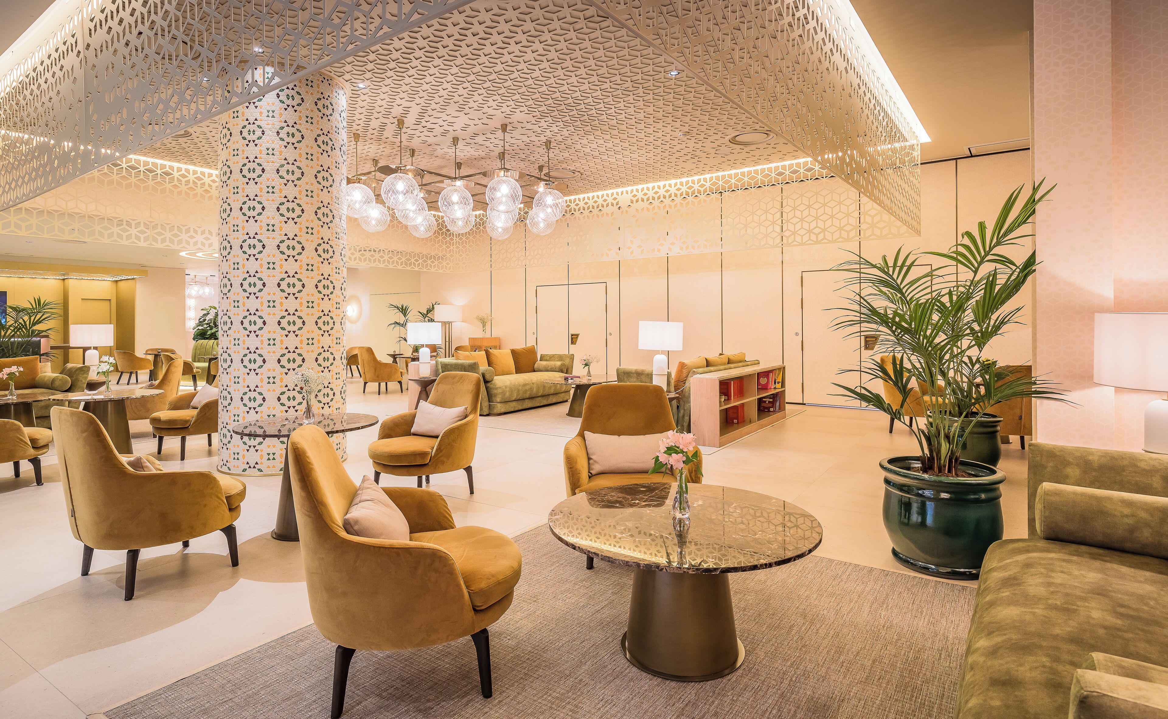 Eine geräumige Lobby mit modernen Möbeln, einer gemusterten Decke und stimmungsvoller Beleuchtung.