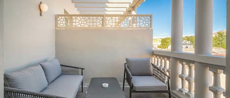 A balcony with a sofa, two chairs, a small table, and a decorative partition.