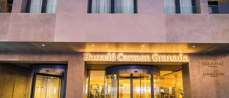 A hotel entrance with a revolving door, glass facade, and illuminated signage reading "Barceló Carmen Granada."