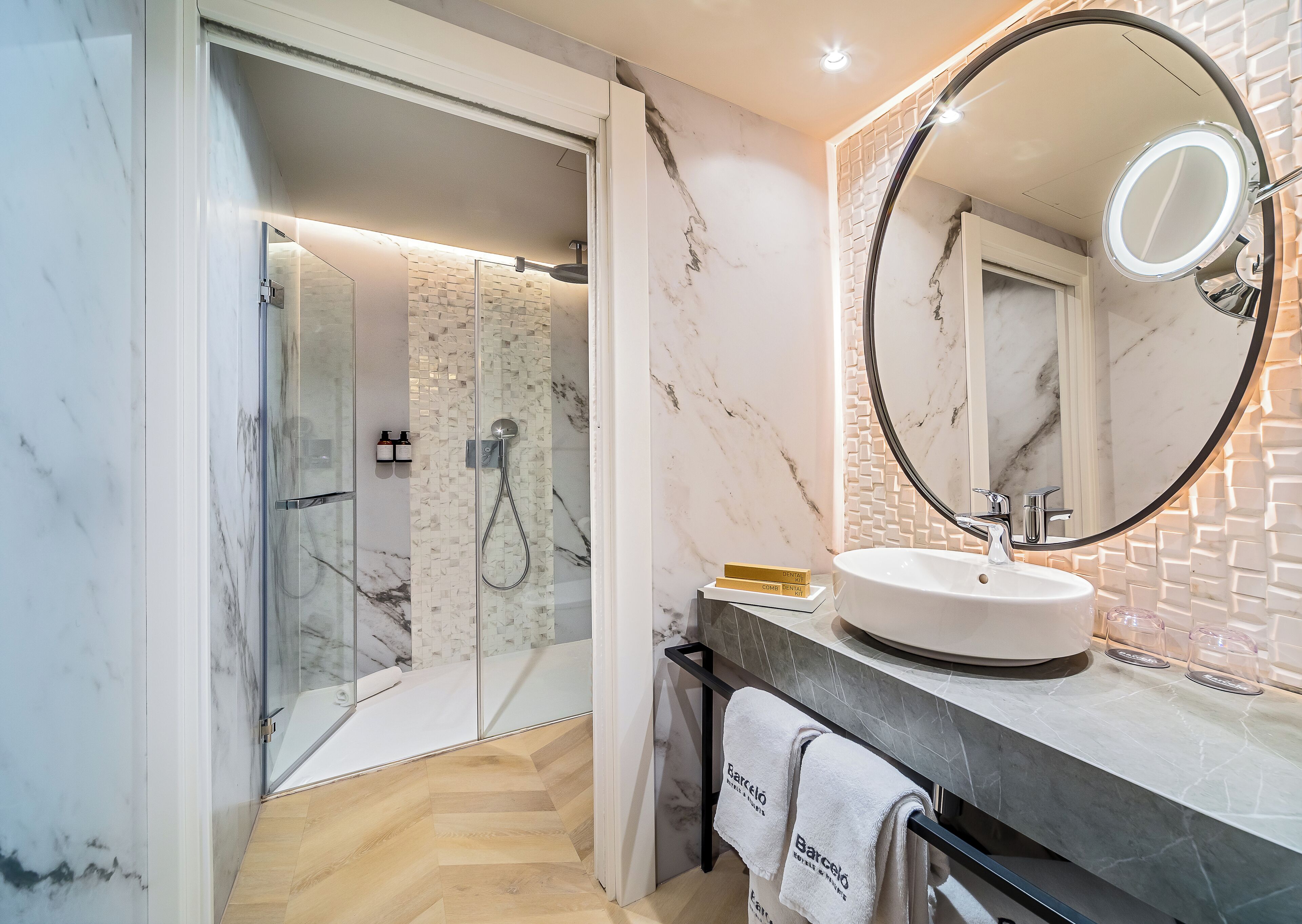 A modern bathroom with a glass-enclosed shower, a round mirror, and a marble-tiled wall.