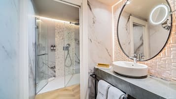 A modern bathroom with a glass-enclosed shower, a round mirror, and a marble-tiled wall.