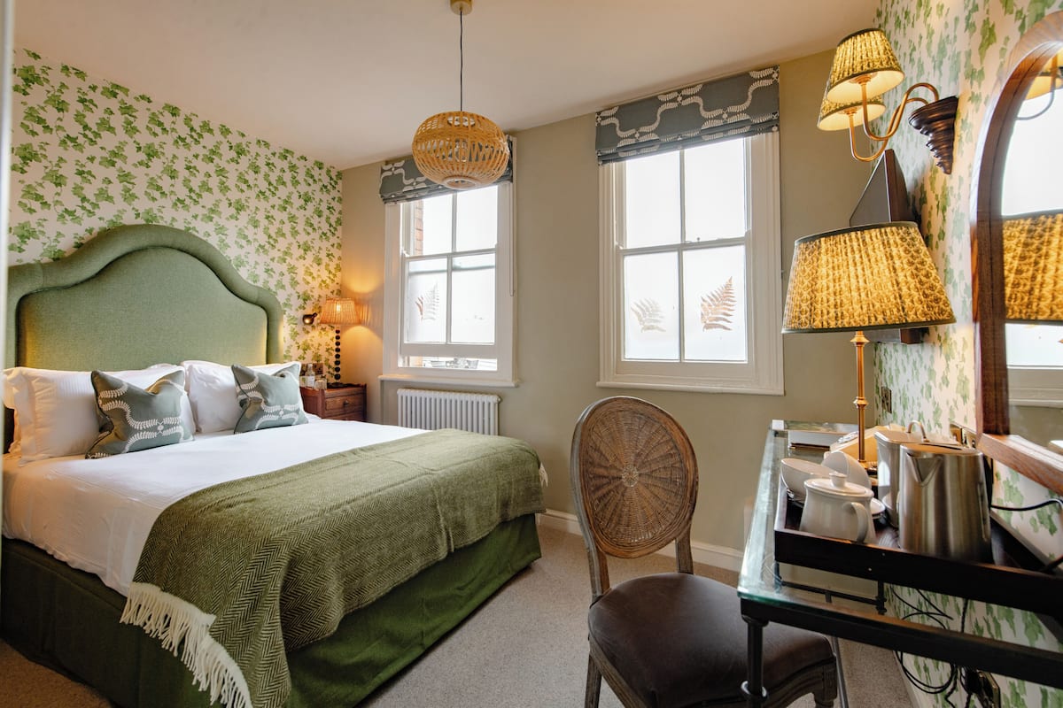Une chambre à coucher comprenant un lit, une table de chevet, une lampe, une chaise et un bureau avec un miroir et une bouilloire.