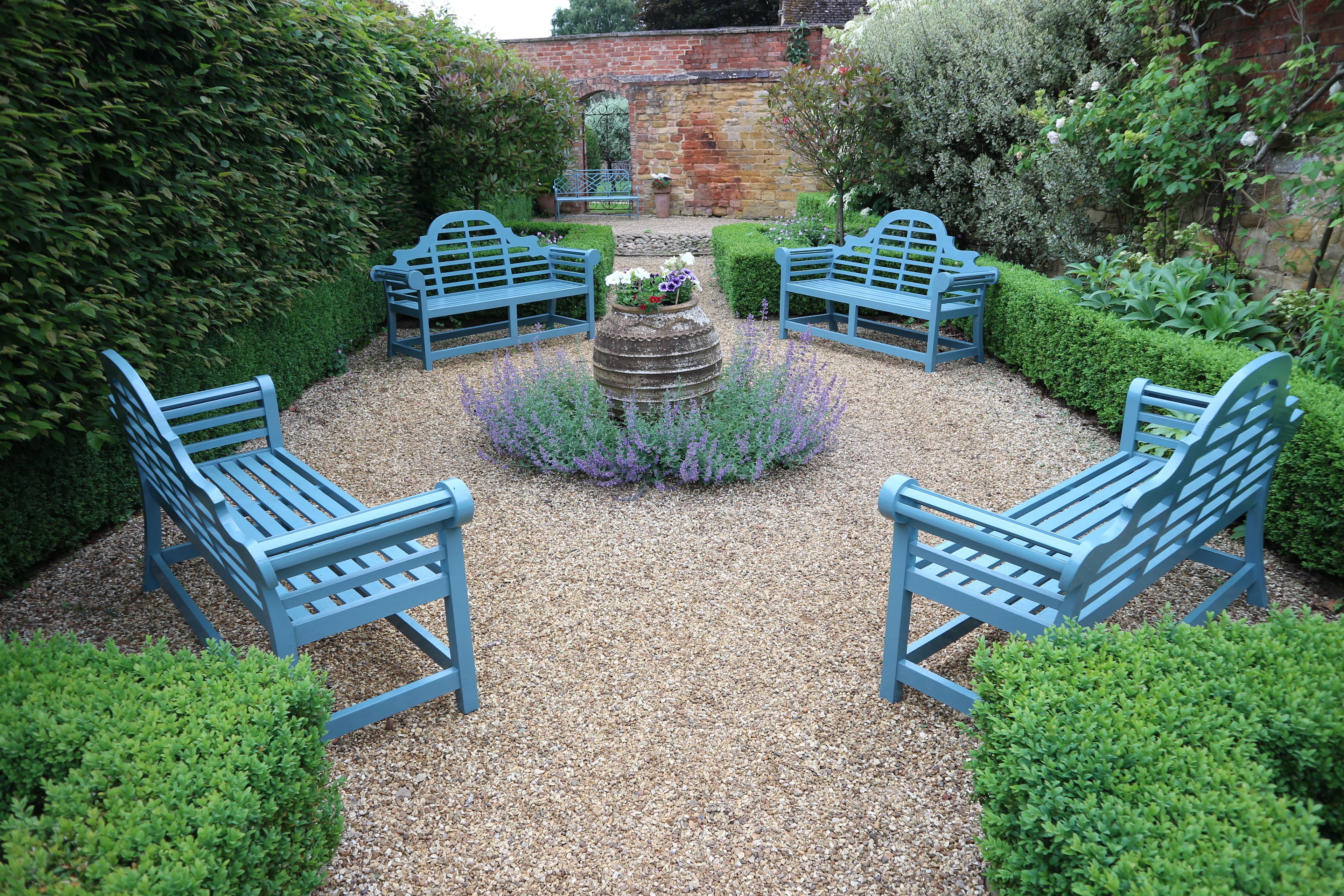 A garden with four blue benches arranged in a circle around a central flower bed.