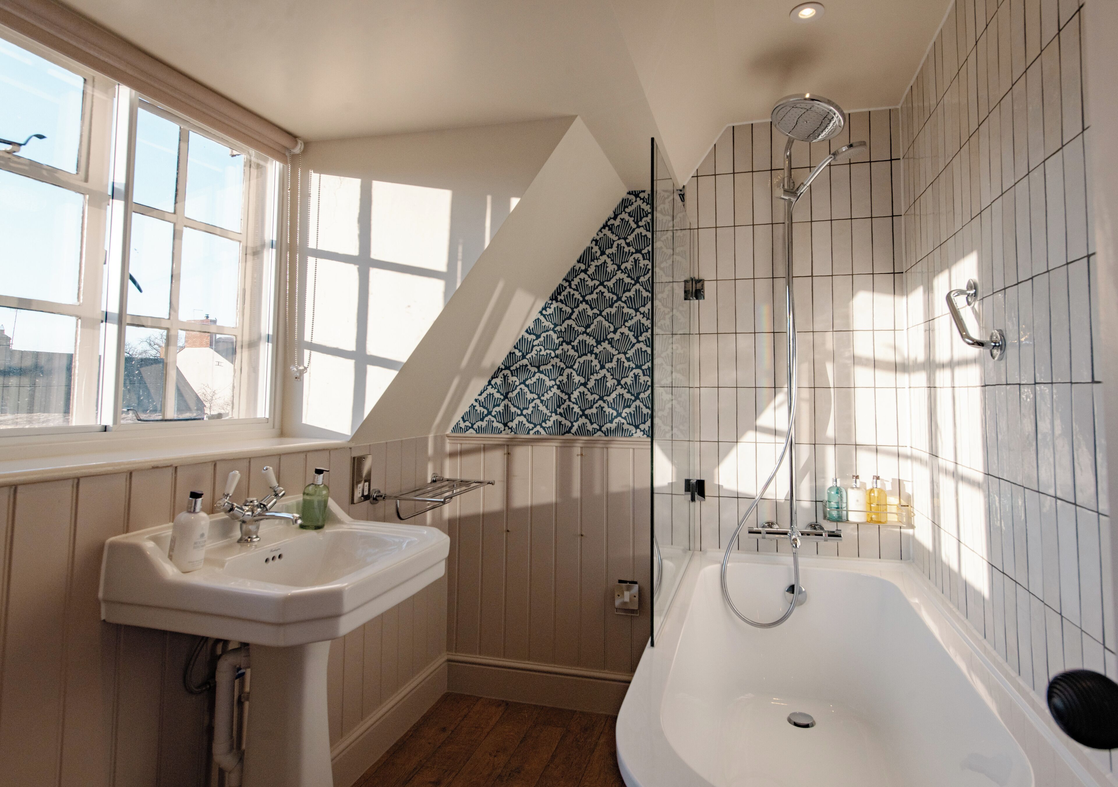 Un bagno con una vasca freestanding, una finestra con persiane, un lavandino con articoli da toilette e uno schienale piastrellato decorato.