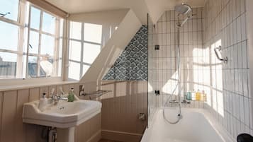 Un bagno con una vasca freestanding, una finestra con persiane, un lavandino con articoli da toilette e uno schienale piastrellato decorato.