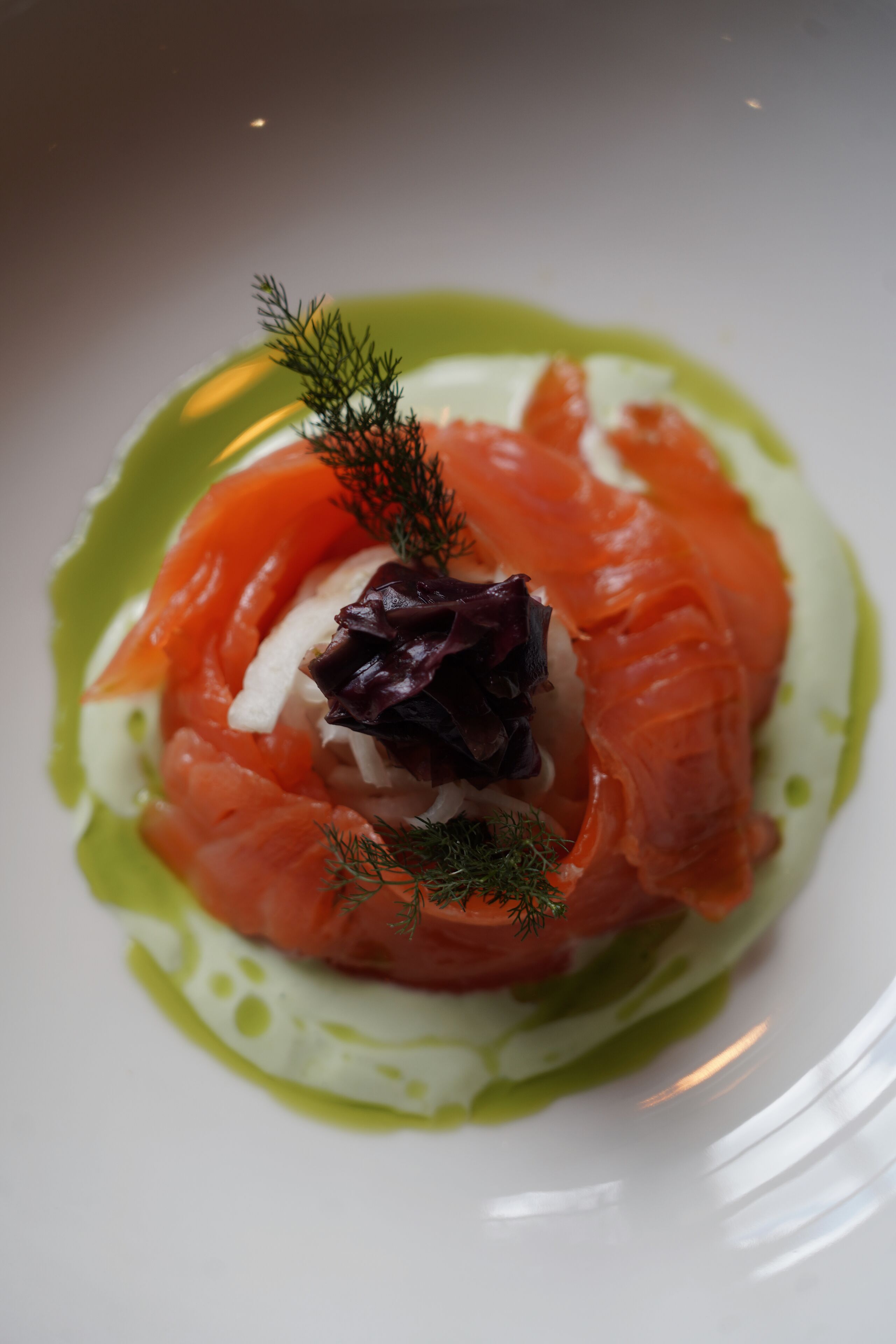 A plate of food with salmon, a dollop of cream, and a garnish of dill.