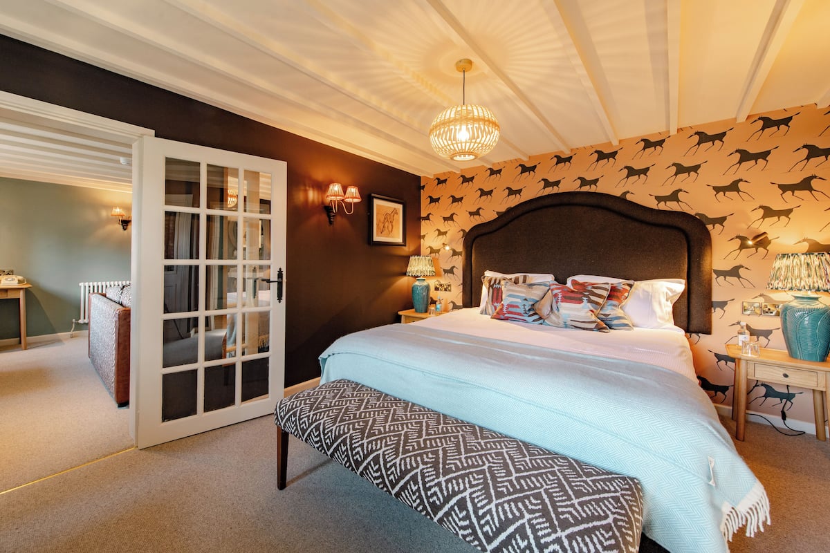 Une chambre avec un grand lit, un banc, une porte donnant sur une autre pièce et un mur orné de motifs animaliers.