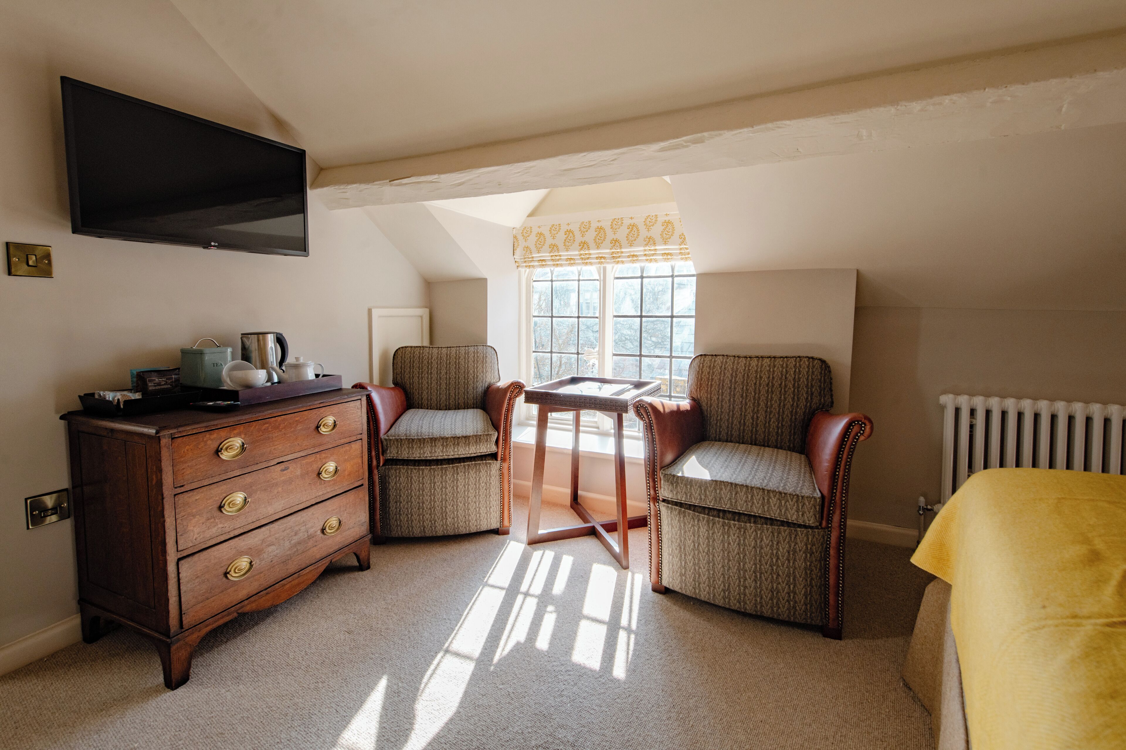 A cozy room with a wooden dresser, two armchairs, a small table, and a television mounted on the wall.