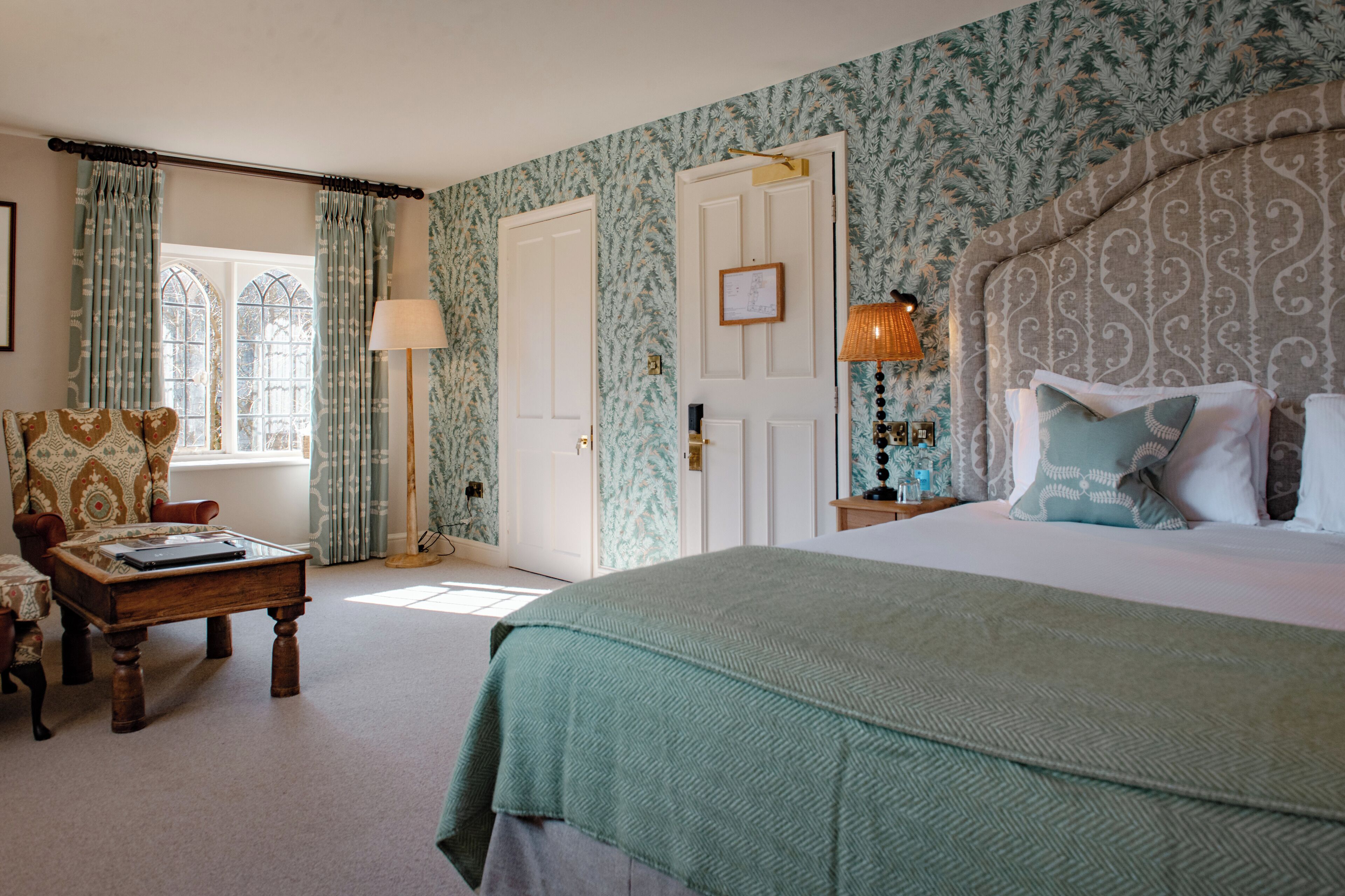 A bedroom with a large bed, a wooden coffee table, a chair, and a nightstand with a lamp.