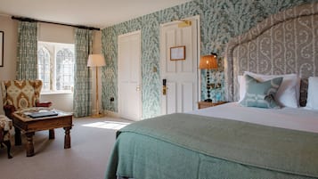 A bedroom with a large bed, a wooden coffee table, a chair, and a nightstand with a lamp.