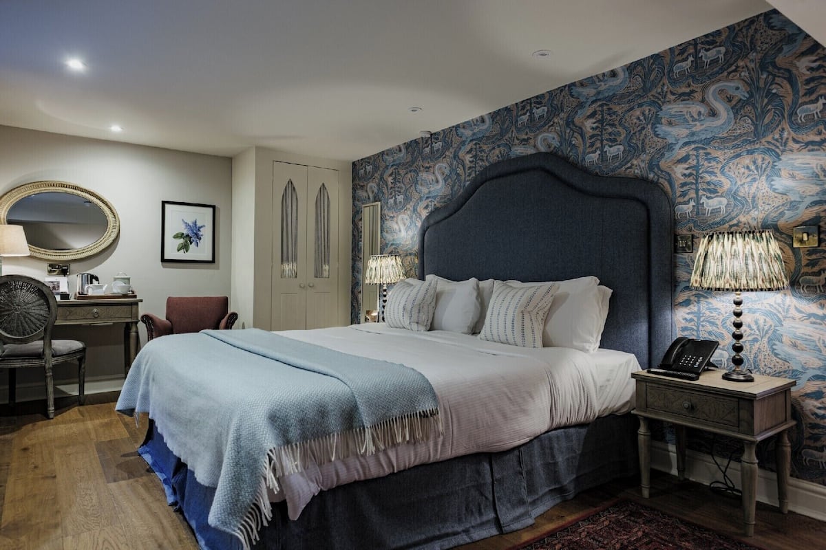 Une chambre avec un grand lit, un bureau, une chaise, une armoire et un mur décoré d’un motif.