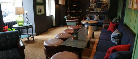 A cozy lounge area with a sofa, ottomans, a table, and a bookshelf.