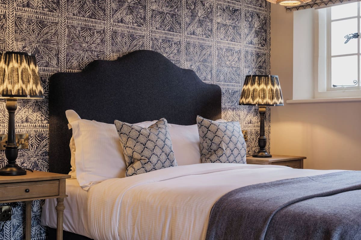 Un lit bien fait, avec une tête de lit sombre, des coussins à motifs et deux lampes de chevet.